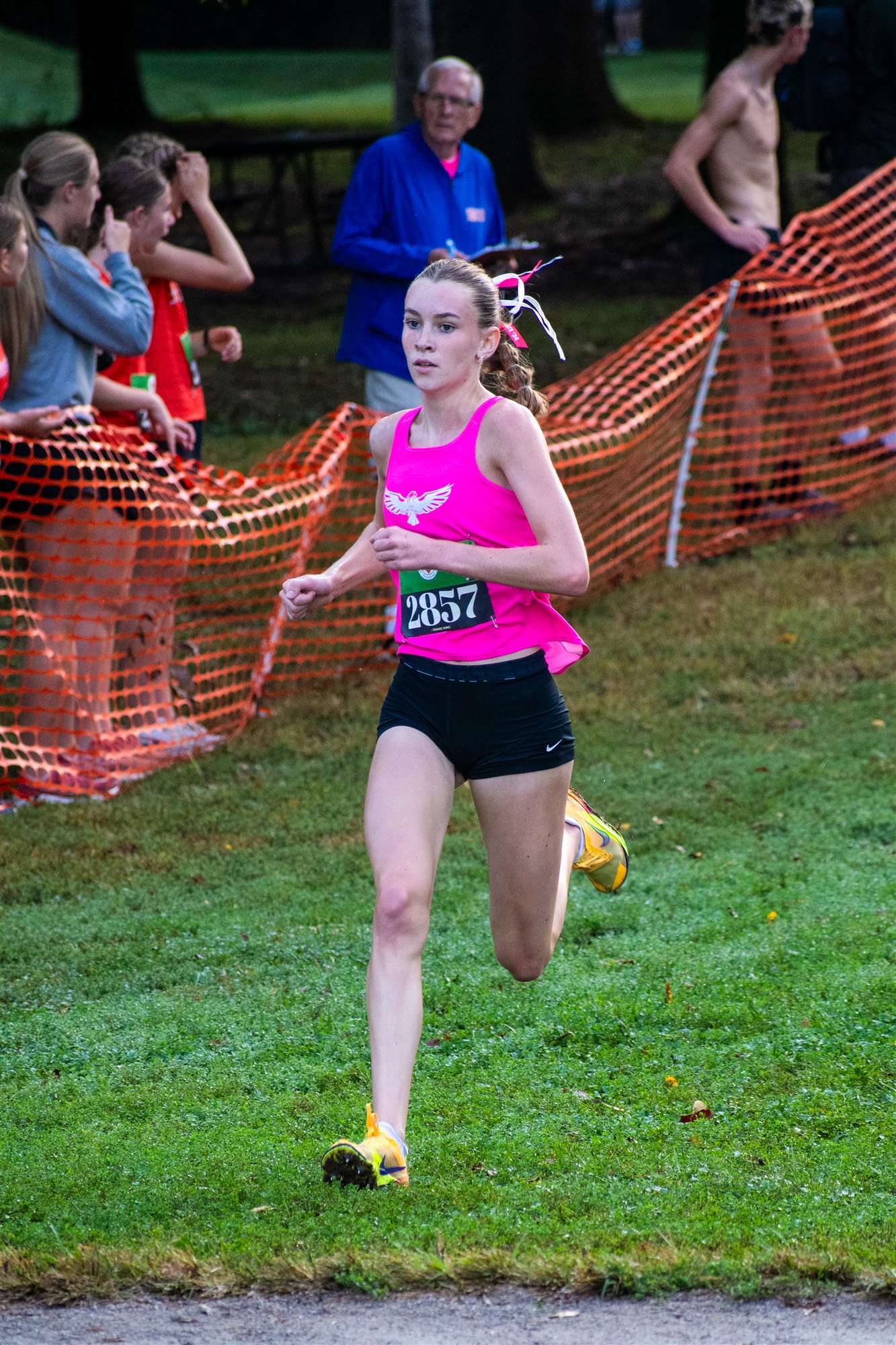 Elle Campbell of Milford runs in a pink jersey, bib 2857, past orange safety fencing during a cross country meet
